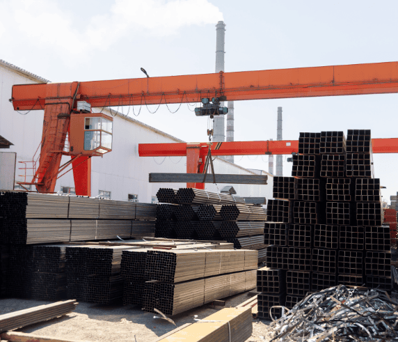 Operate a Bridge and Gantry Crane. An overhead crane lifting heavy steel materials at an industrial manufacturing yard.