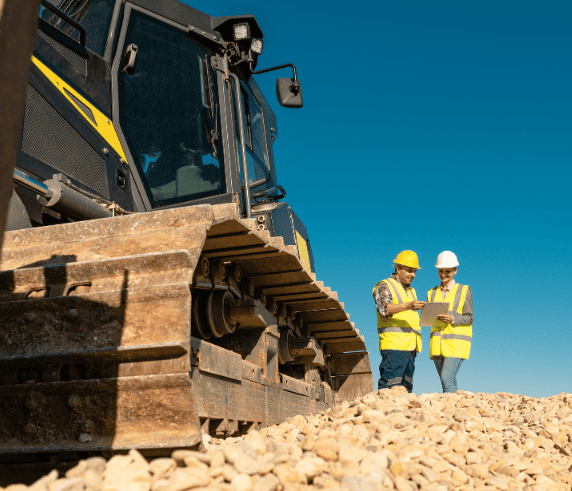 Professionals attending the Section 26 Course Perth for statutory supervisor roles. Statutory Supervisor WHS Risk Management. Two construction supervisors wearing yellow safety gear and helmets reviewing documents beside a large tracked excavator on a gravel site.
