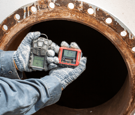 Gas Safety personnel holding up a gas tester Infront of an open gas pipeline performing a GAS TEST